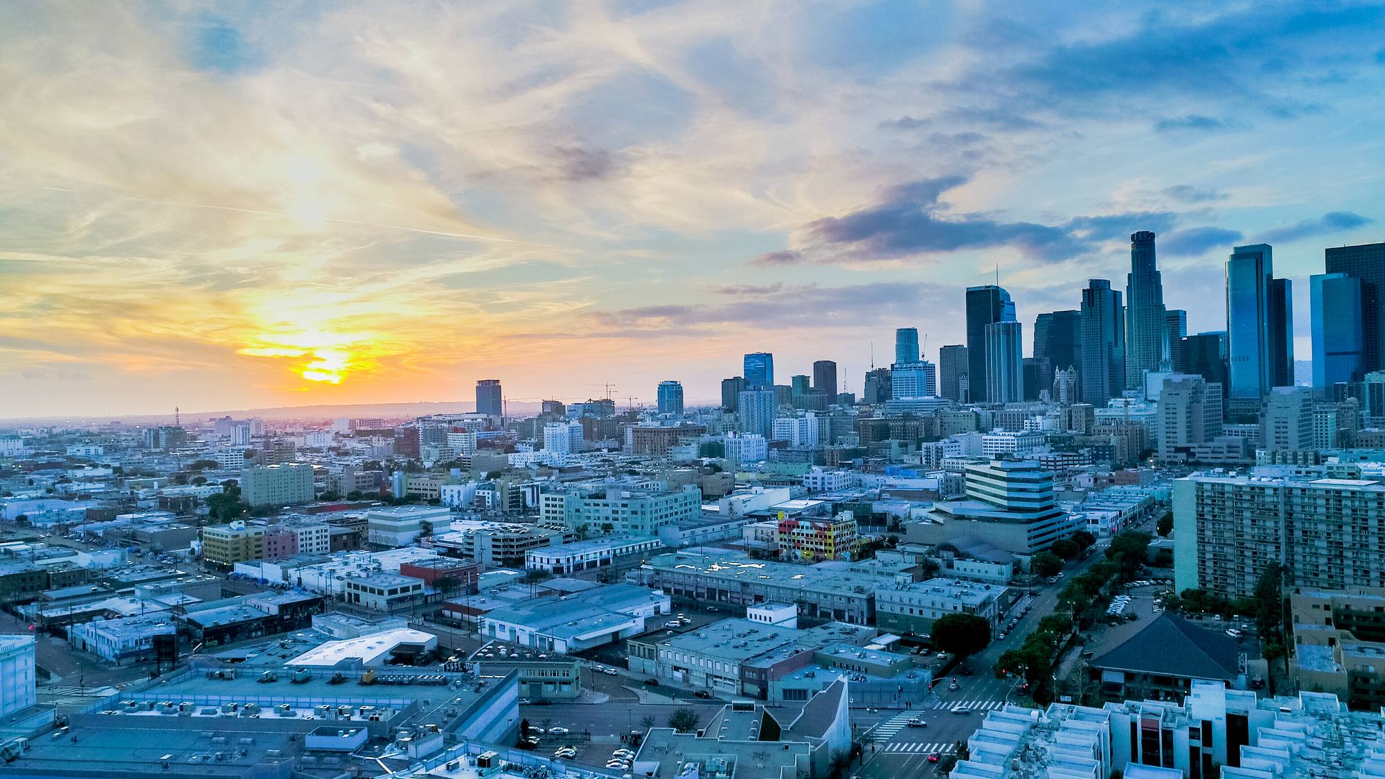 A city skyline and surrounding neighborhoods beneath a sunset sky