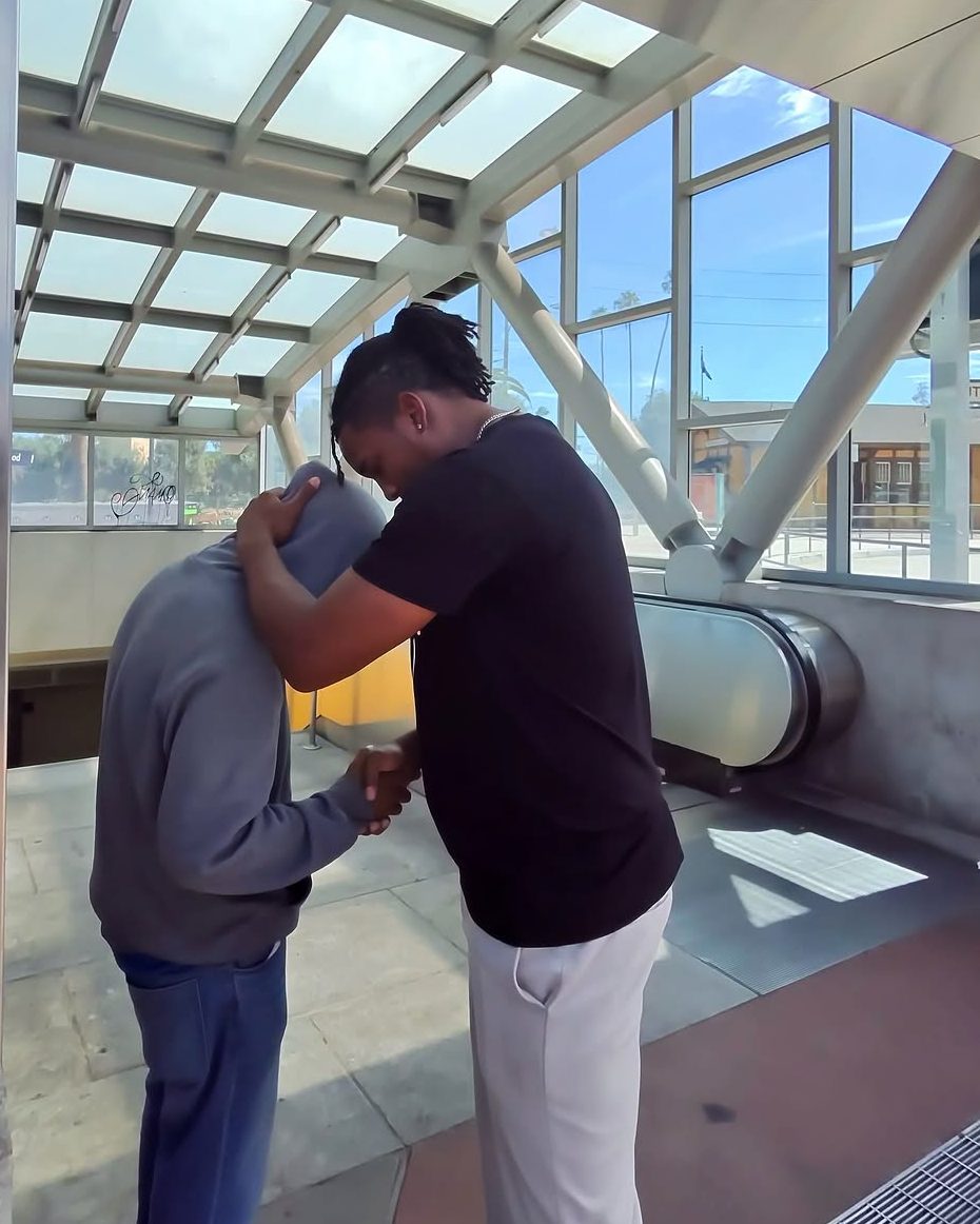 A church member praying with a man at a transit station, a hand on his shoulder
